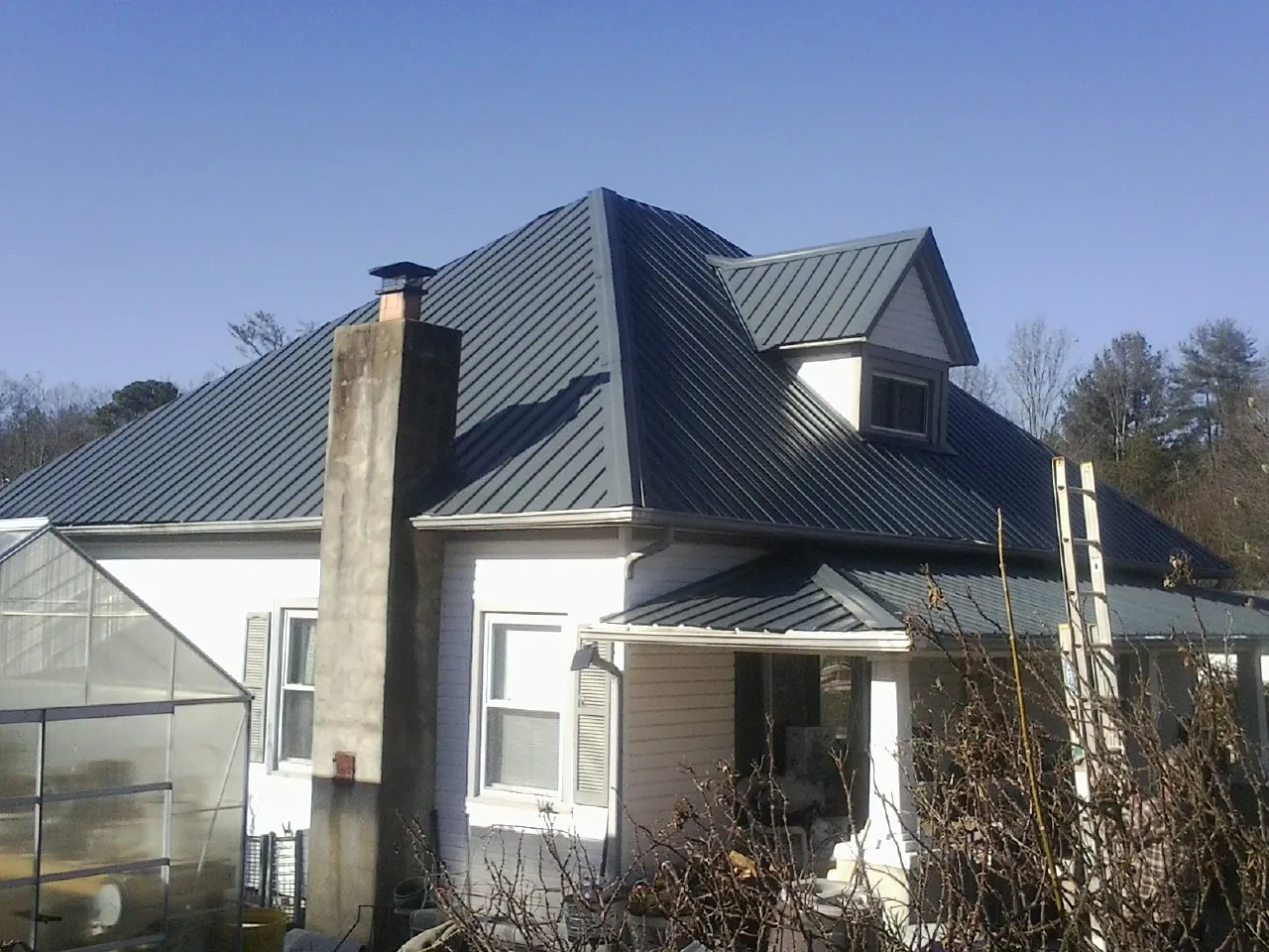 Dark blue standing seam metal roof on a white farmhouse with dormer — Slate & Tile Roof Repair by Roofing Brothers in Casco
