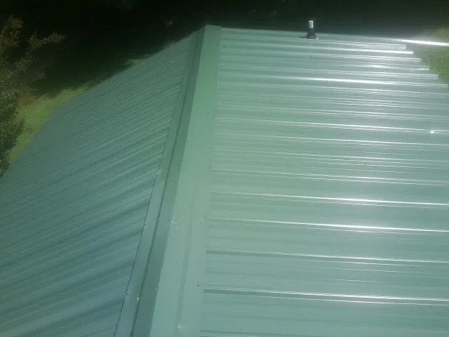 New green metal panels meeting at the ridge of a roof — Flat Roof Repair work by our crew in Casco