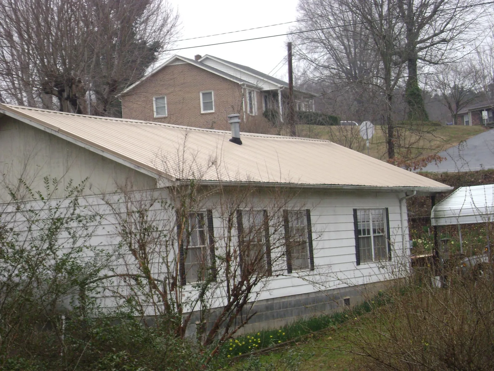 Tan metal roof on a white sided house set into a hillside — Commercial Roofing by Roofing Brothers in Casco
